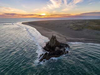 Coastal sunset view of a rocky outcrop with a lighthouse. Waves crash against the rocks at the edge of a sandy beach. Dramatic colors. WHATIPU, AUCKLAND, NEW ZEALAND