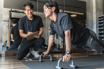 Obraz premium スポーツジムでパーソナルトレーニングを受ける若いアジア人男性 