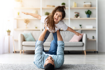 Happy middle-eastern dad and daughter playing airplane together at home, young arab father lifting...