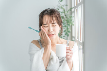 虫歯が痛い・しみて頬を押さえるアジア人女性
