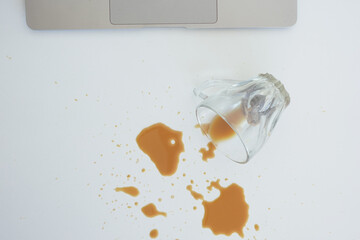 A drink was accidentally spilled on a desk with a laptop and glasses, creating a mess