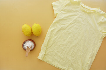 Baking soda, lemon and a shirt on yellow background 