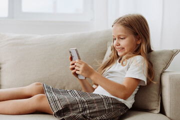 Young girl in plaid skirt engrossed in cell phone on cozy couch