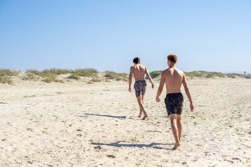 Fototapeta premium Two young people in swimwear strolling along the beach, exuding tranquility and relaxation, enjoying their vacation by the sea.