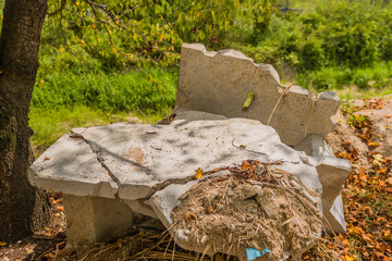 Broken concrete bench partially buried in autumn leaves under tree foliage with natural scenery in the background, in rural South Korea