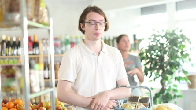 In shop girl stands behind husband, hurling abuse and indignation at him. In trading floor, sullen man stands with shop basket, swears with wife and listens to womans accusations. 