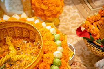 A golden offering tray decorated with marigold flowers, lotus buds, and sacred items for a traditional Thai religious or cultural ceremony.