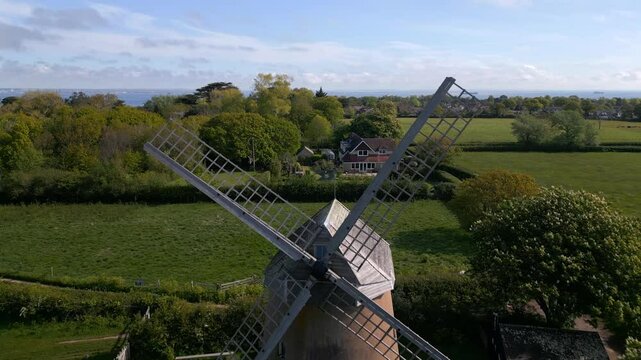 Forward drone shot flying between Bembridge Windmill blades, rising to reveal the stunning coastline, sea views, and picturesque village landscape on the Isle of Wight.