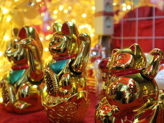 Fototapeta premium A close-up shot of several golden Maneki-neko waving cats with blurred bokeh lights in the background.