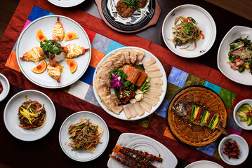 A table with dried pollack, boiled pork, kimchi, steamed fish, grilled shrimp with cheese, and various side dishes