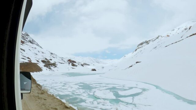 4K shot of Frozen Suraj Tal lake during winter season at Lahaul, Himachal Pradesh, India. Cold frozen lake in Himalaya mountains. Lake surrounded with snowcapped mountains. View from moving car.
