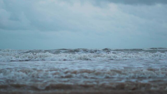 Sea waves on sandy beach with clouds in sky at Mandvi, Kutch, India. Calm coastline with dark cloudy sky. Tropical vacation, beach holidays concept. 