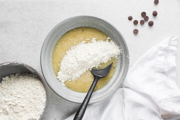 Overhead view of flour being folded into cookie dough, top view of cookie dough being mixed in a grey bowl, process of making cookie dough or chocolate chip cookie dough