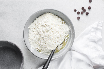 Overhead view of flour being folded into cookie dough, top view of cookie dough being mixed in a grey bowl, process of making cookie dough or chocolate chip cookie dough