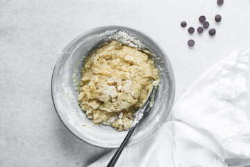 Overhead view of flour being folded into cookie dough, top view of cookie dough being mixed in a grey bowl, process of making cookie dough or chocolate chip cookie dough