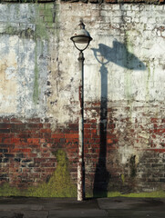 Old street lamp against a weathered brick wall with green moss.