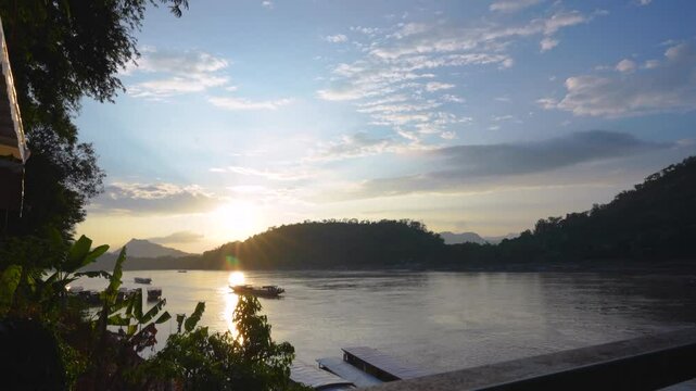 A serene timelapse of touring boats on the Khan River in Luang Prabang during sunset, with golden light reflecting on calm waters and lush hills, capturing the peaceful beauty of Laos.