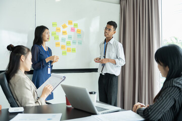 Asian people using sticky notes on a task board, brainstorming idea in modern office
