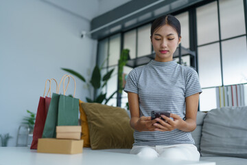 Asian woman sitting on sofa with shopping bags on table her using smartphone shopping online in living room at home