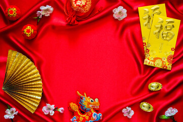 Chinese new year background with envelope packets or ang bao (word mean blessing), red bag and ingots (words mean wealth), hanging pendant dragon on red cloth background.