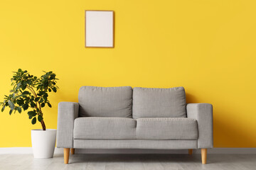 Grey sofa with plant and blank frame on yellow wall in living room