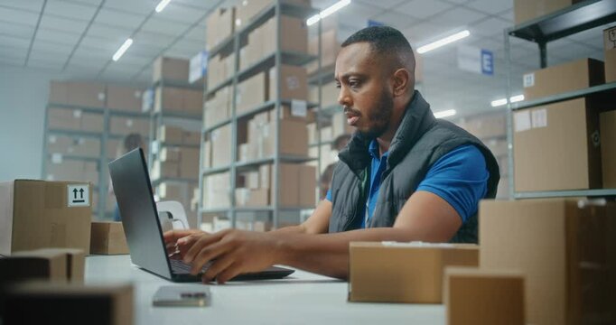 African American post office employee scans parcels with barcode scanner, enters data on laptop. Sorting center workers checking and carrying boxes for delivery to customers. Warehouse of online store