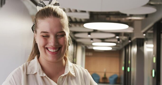 Smiling woman in office hallway, wearing white shirt and striped hair bow
