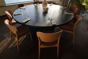 round table chair napkin restaurant Dining room with a circular black table, wood chairs, and plant in pot. interior design concept. sunlight from windows.