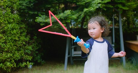 A little Asian child enjoys Playing blowing Colorful soap bubbles Having Fun in a Lush Green Garden surrounded by greenery and sunlight on a Sunny Day, capturing the essence of carefree childhood fun.
