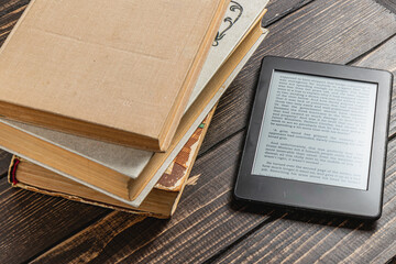 Reading an electronic book beside old books on a wooden table near a window