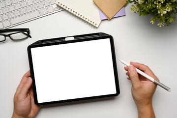 Hands holding a digital tablet with blank white screen at clean and minimalist workspace