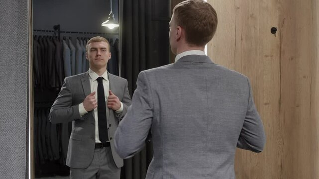 Elegant businessman admiring his reflection in a mirror while trying on stylish new suit in clothing store during exciting shopping session for formal attire