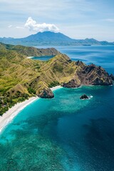 Obraz premium Beautiful aerial view of an Indonesian island with green mountains and a blue ocean, featuring white sandy beaches, cliffs, and sea waves.