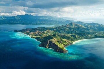 Beautiful aerial view of an Indonesian island with green mountains and a blue ocean, featuring white sandy beaches, cliffs, and sea waves.