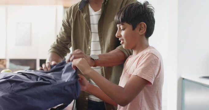 Indian father packing backpack while young son smiling and standing nearby