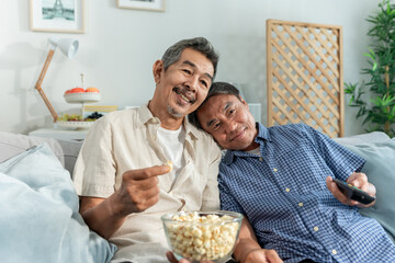 Asian two elderly man friend watching television together in house. 