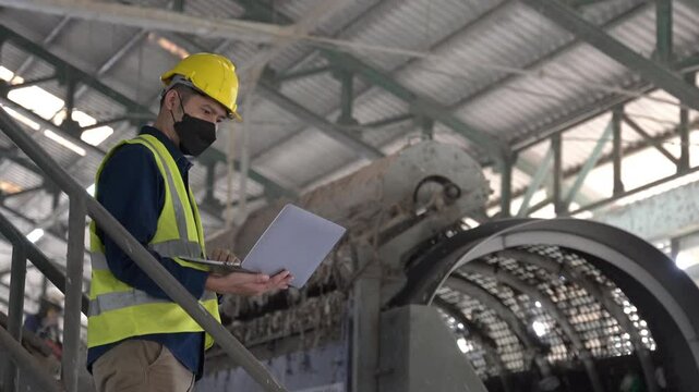 An Engineer working on a laptop surrounded by industrial recycling machines, analyzing data and optimizing processes in waste separation plant.