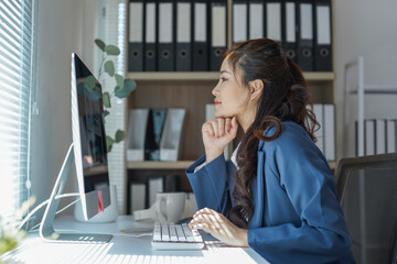 Young businesswoman sitting at her desk and working on desktop computer in modern office, she is...