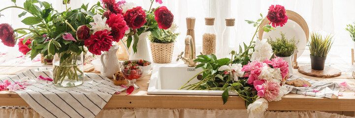 The kitchen countertop is decorated with peonies. The interior is decorated with spring flowers. Pink peonies and sweet cupcakes on a wooden countertop. Interior details.