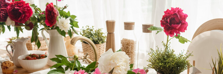 The kitchen countertop is decorated with peonies. The interior is decorated with spring flowers. Pink peonies and sweet cupcakes on a wooden countertop. Interior details.