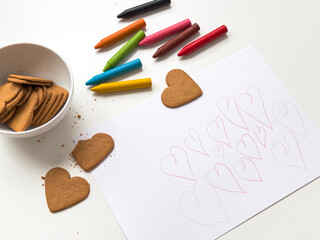 Heart shaped cookies with crayons and heart drawings on white paper