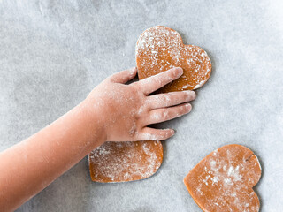 Childs hand decorating heart shaped cookies on baking sheet