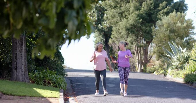 Multiracial female friends walking and talking on suburban street, outdoor exercise, copy space