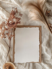 Blank stationery mockup with dried flowers and feathers on a textured fabric background. Perfect for wedding invitations or announcements.