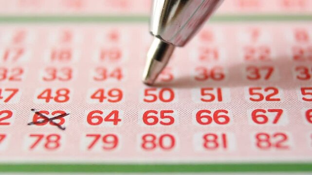 A man marks with a pen numbers 63, 50, 52 on a lottery ticket. The rows of red numbers on the white lottery ticket are arranged horizontally. Close-up horizontal video