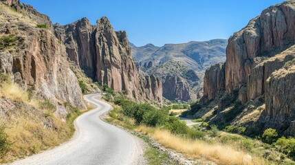 A winding road through a canyon, surrounded by towering rock formations under a cloudless sky.