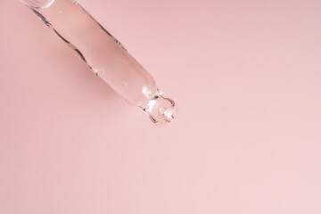 A closeup of a liquid filled dropper against a pink background, highlighting its beauty