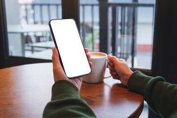 Mockup image of a woman holding mobile phone with blank desktop screen while drinking coffee in cafe