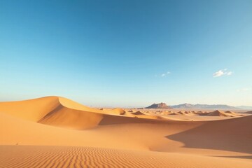 Vast expanse of sun-kissed sand dunes stretching to distant, rocky mountains under a clear, azure sky