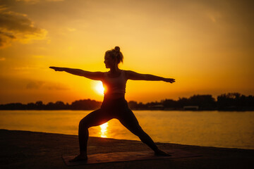 Woman practicing yoga in sunset. Virabhadrasana, Warrior 2 pose.